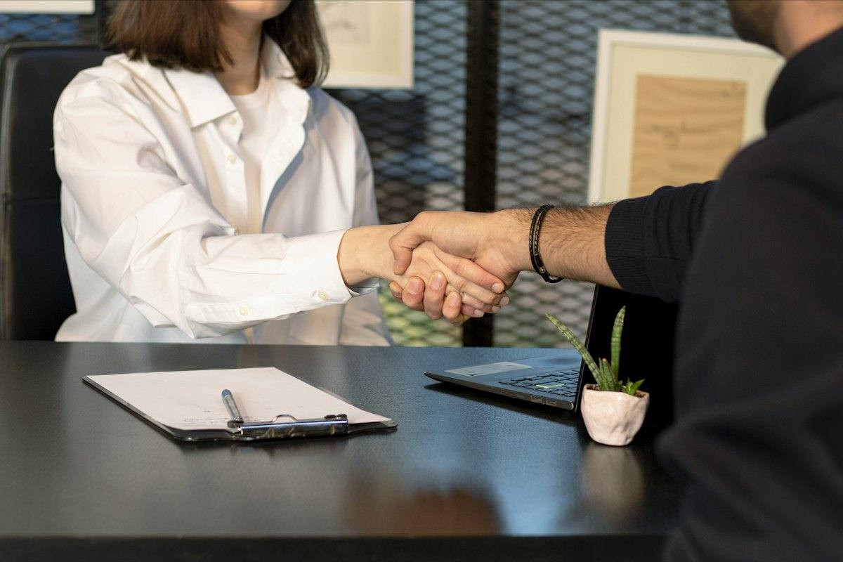 A broker shaking hands with a client across a desk